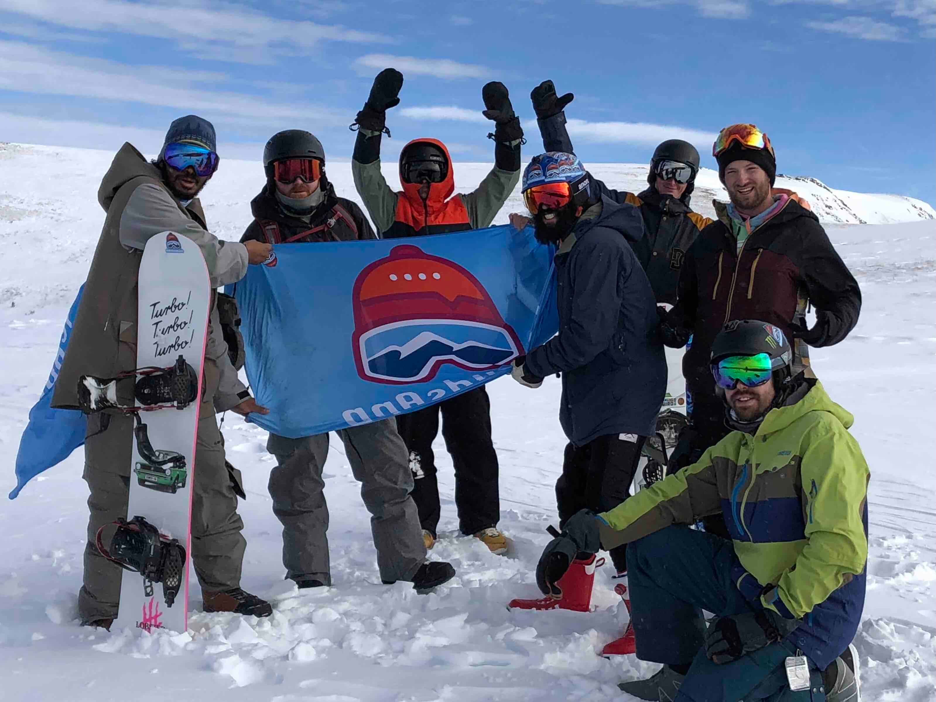 A group of SkiBuds riders together on the mountain holding a SkiBuds flag